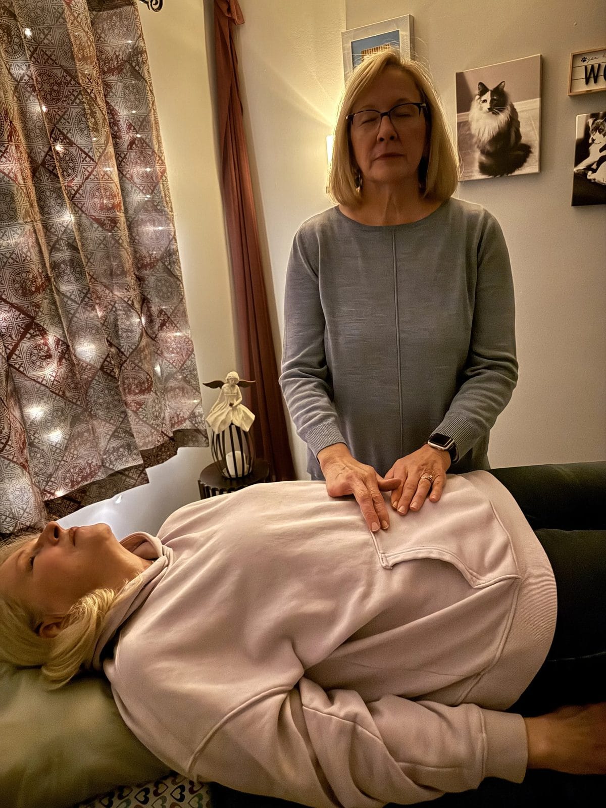 Heather standing beside her Reiki table with her hands resting gently over a client