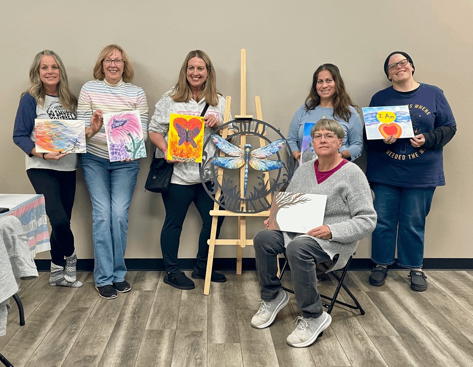 A smiling group holding up the paintings they made at one of Heather's workshops